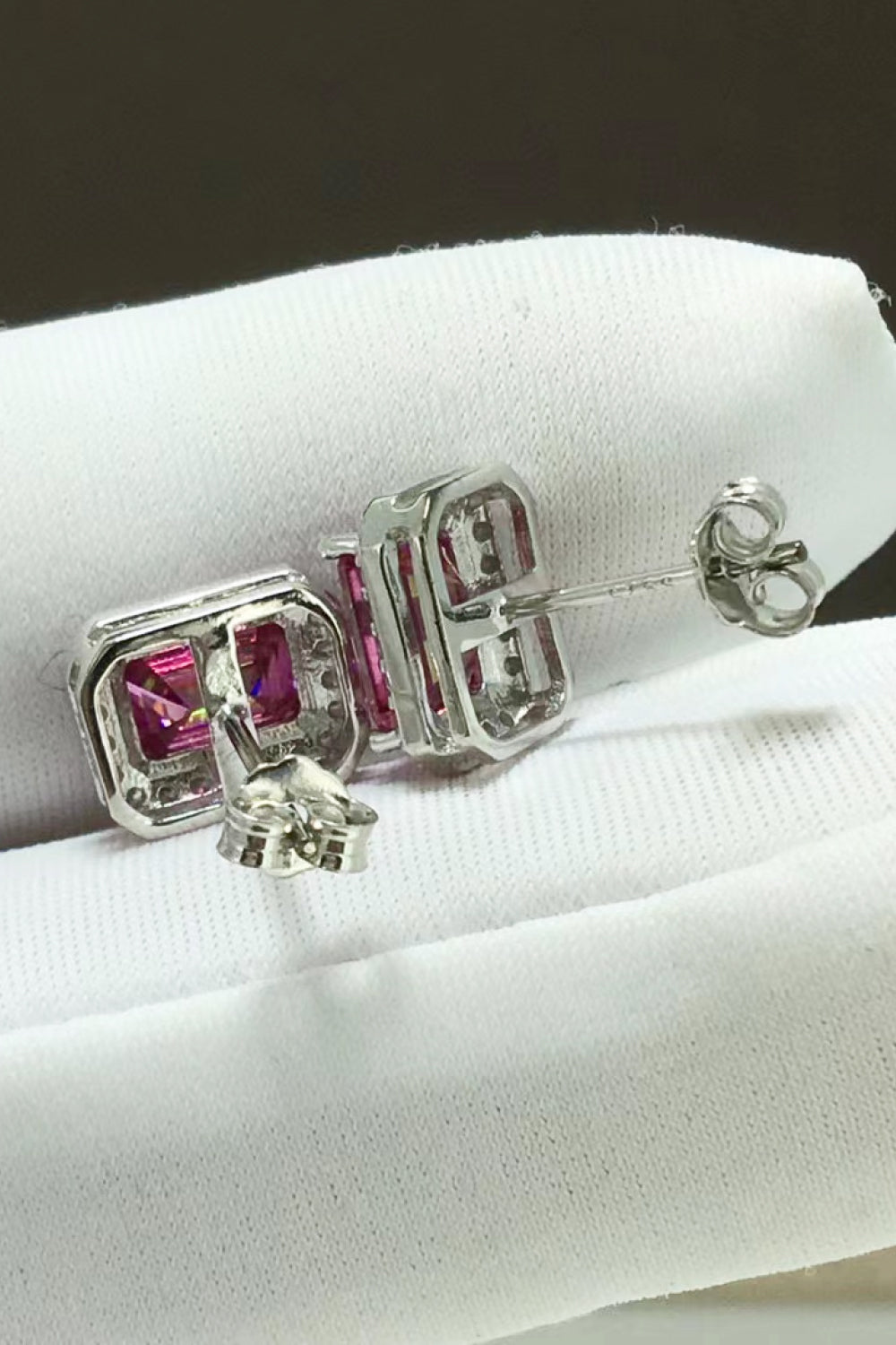 Silver earrings with pink gemstones on a white cushion