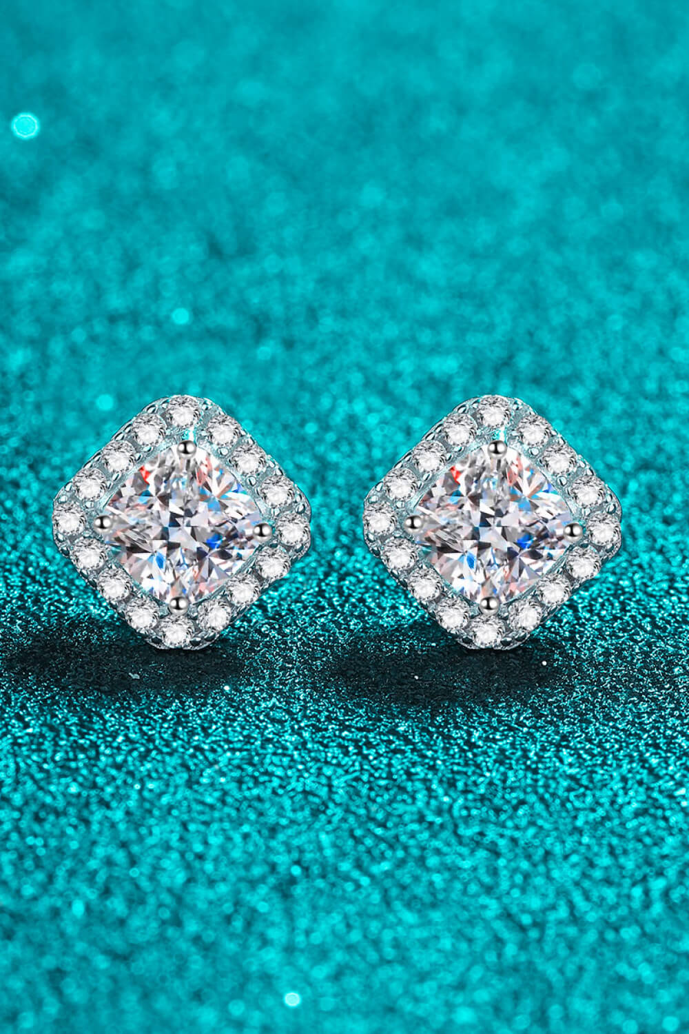 Pair of diamond stud earrings on a teal glitter background