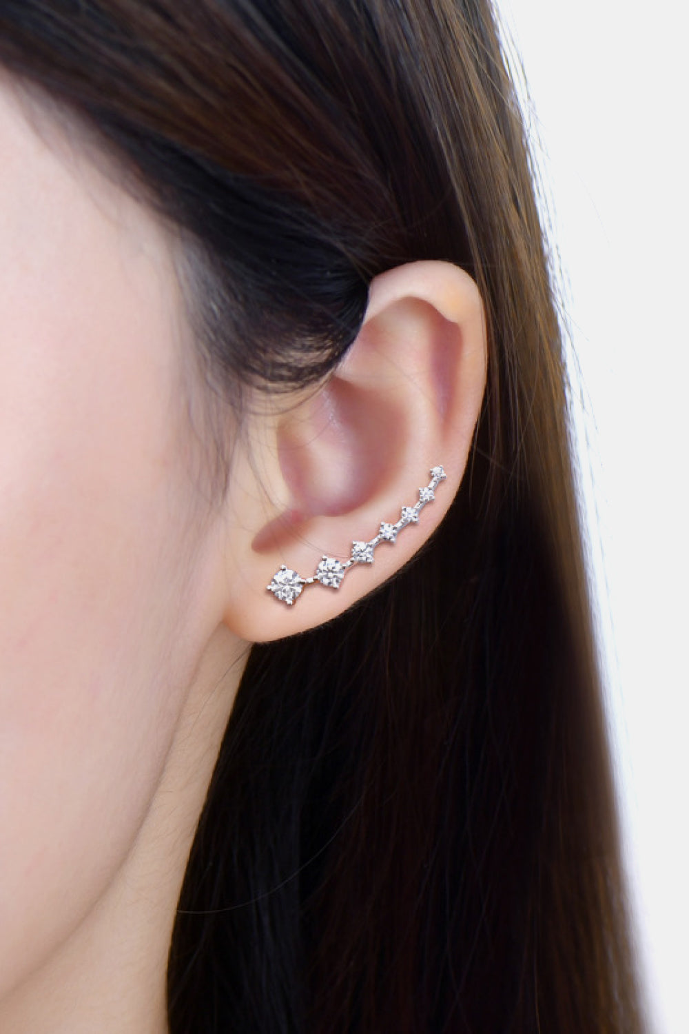 Close-up of an ear wearing a set of silver earrings with small stones.