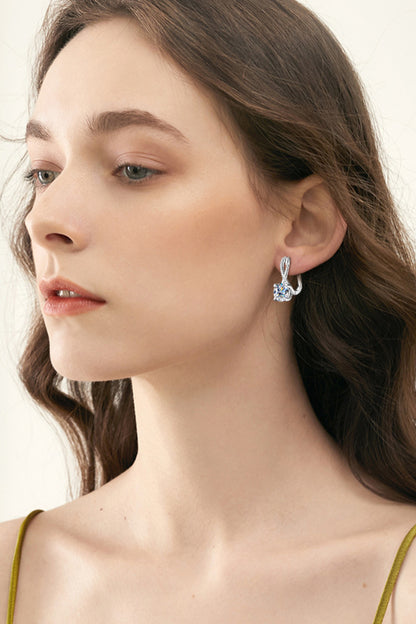Close-up of a woman wearing a silver earring with a clear gemstone against a neutral background