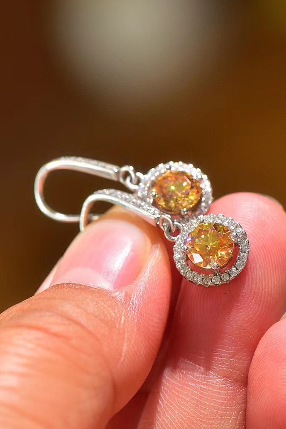 Close-up of a pair of yellow gemstone earrings held between fingers with a blurred background.