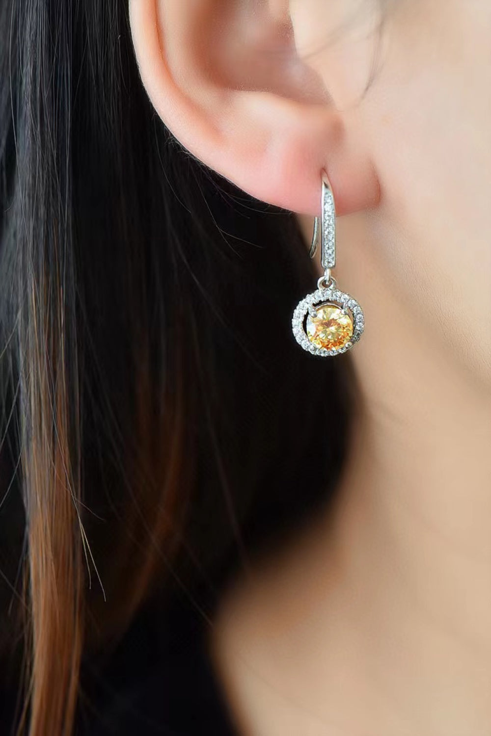 Close-up of a person wearing a sparkling earring with a yellow gemstone.