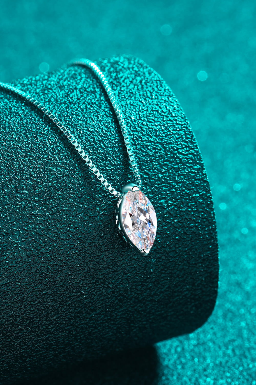 Diamond necklace on a green textured surface with a teal background
