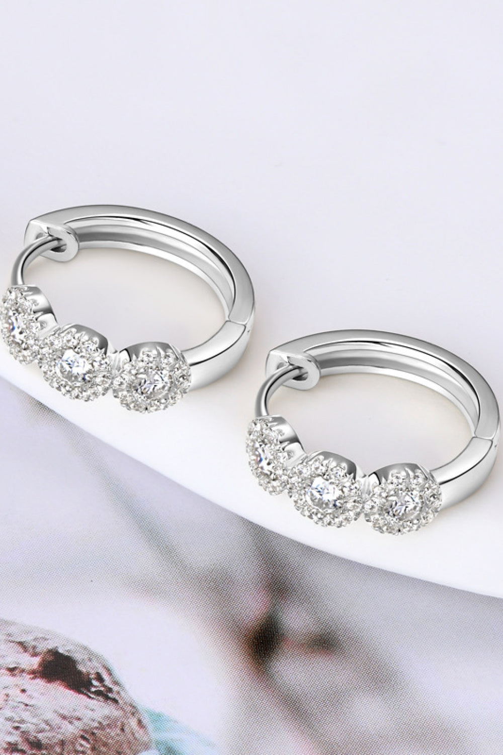 Silver hoop earrings with clear gemstones on a white surface.