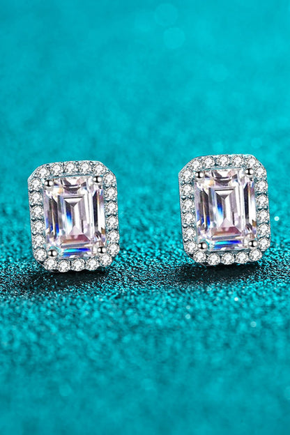 Pair of emerald-cut stud earrings with diamond halo on a teal background