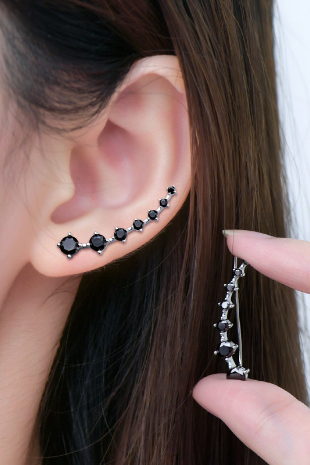 Close-up of an ear with black stud earrings and a hand holding a matching earring.