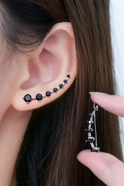 Close-up of an ear with black stud earrings and a hand holding a matching earring.