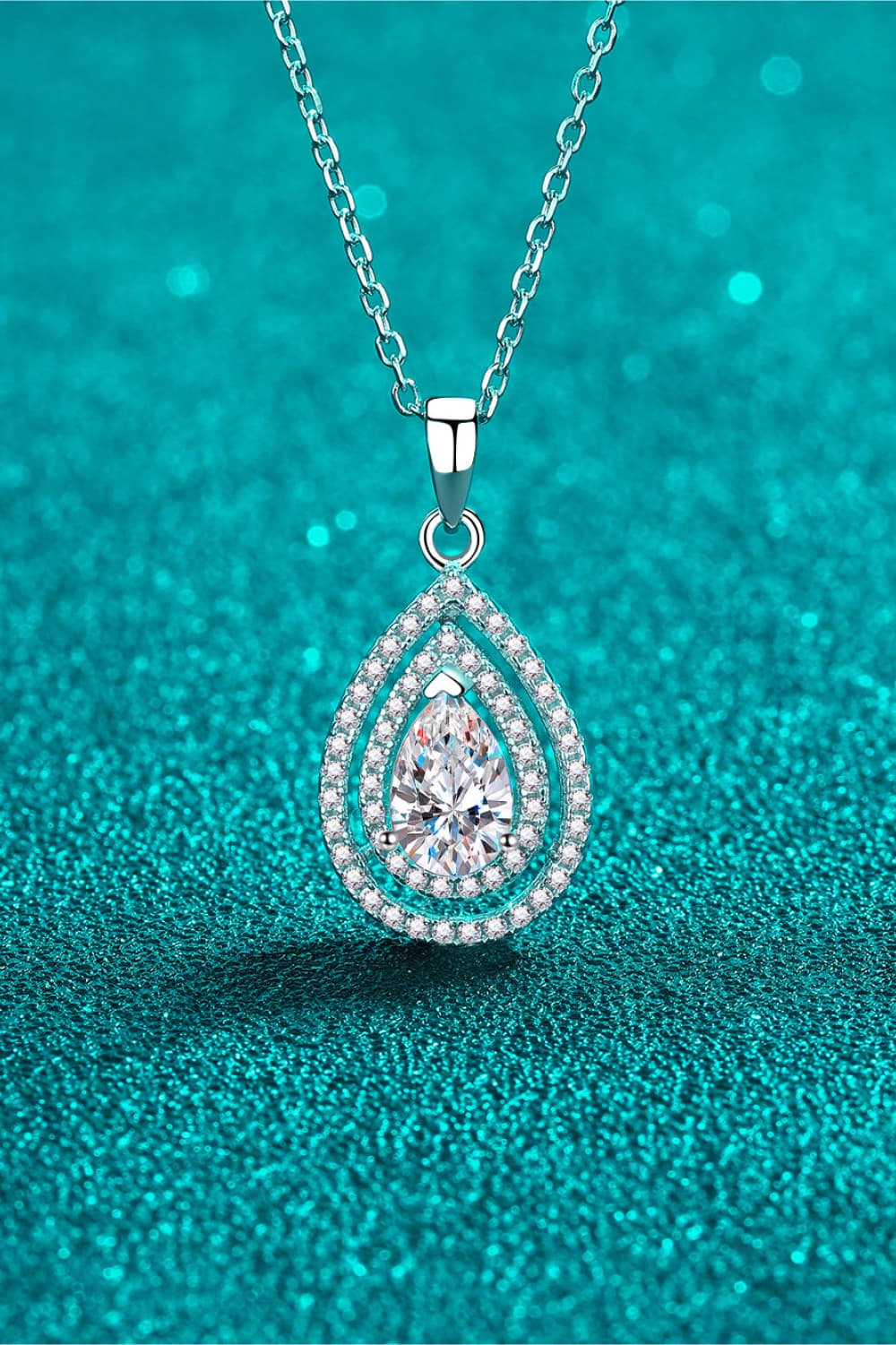 Teardrop-shaped diamond pendant on a chain against a teal background