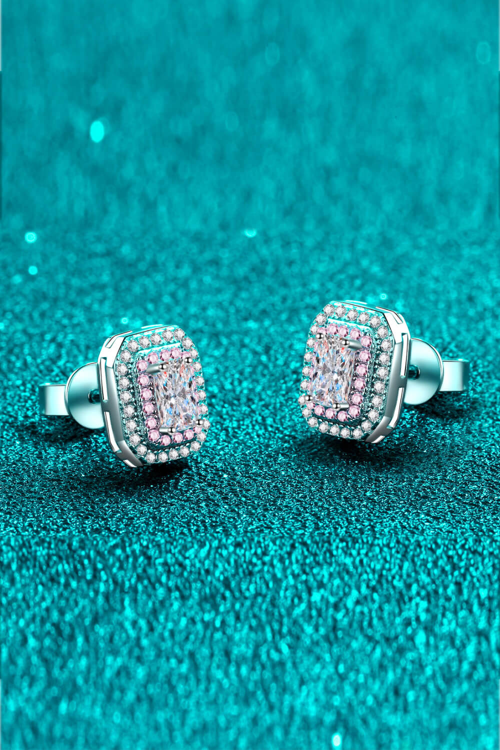 Pair of silver earrings with pink gemstones on a teal glittery background