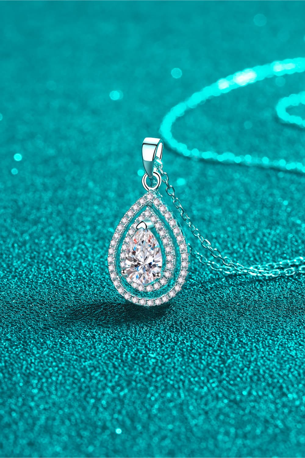 Teardrop-shaped silver pendant with clear gemstone on a teal background