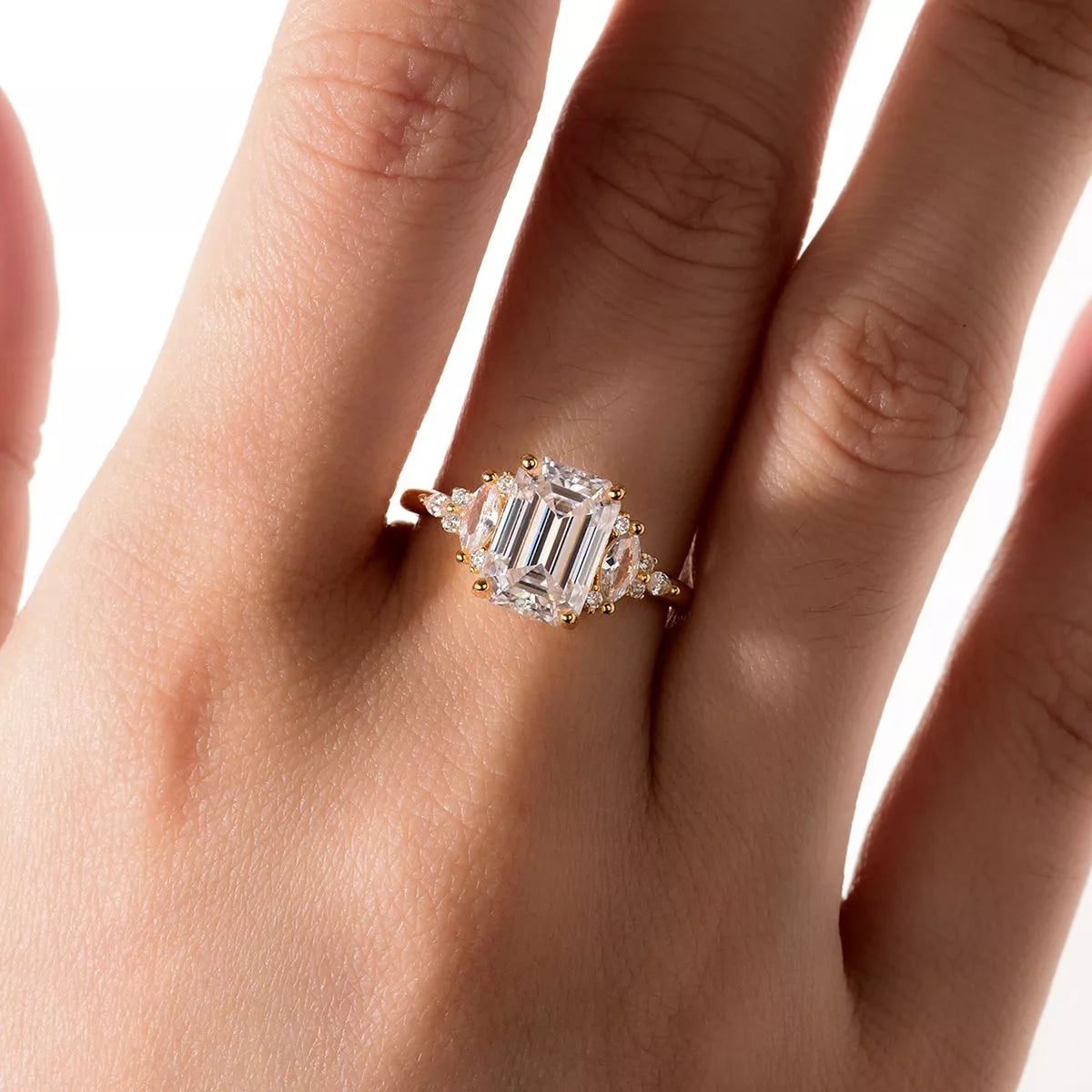 gold ring with emerald-cut diamond on a hand against a white background