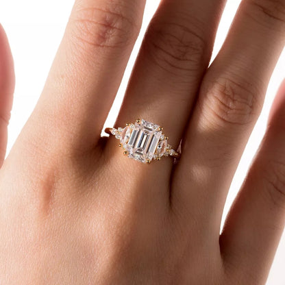 gold ring with emerald-cut diamond on a hand against a white background