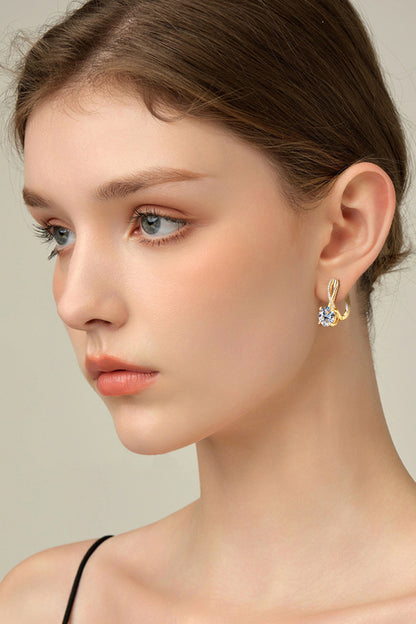 Close-up of a woman wearing a gold earring with a clear gemstone on a neutral background