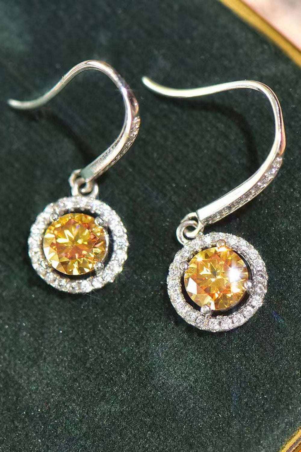 Pair of silver earrings with yellow gemstones on a green background