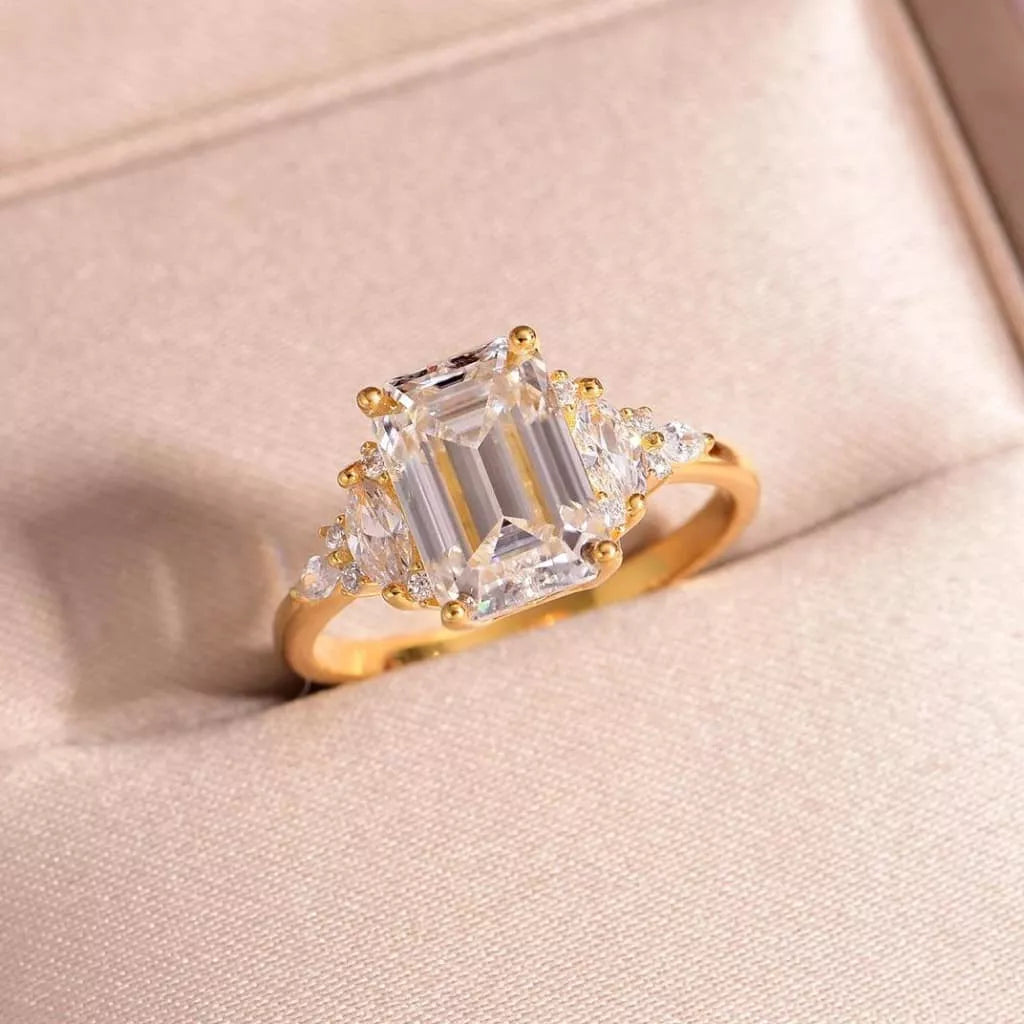 Gold ring with emerald-cut diamonds on a soft pink background