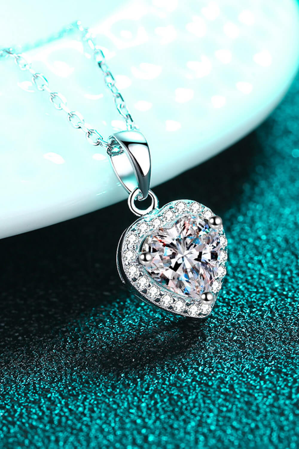 Heart-shaped diamond pendant on a chain against a teal background