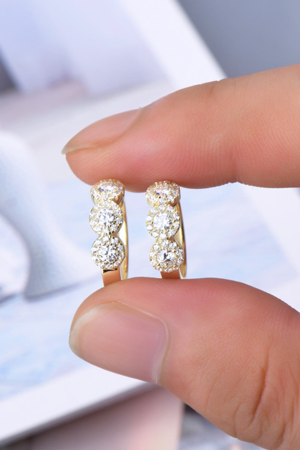 Gold hoop earrings with clear stones held between fingers against a blurred background