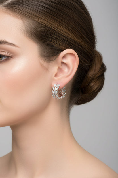 Close-up of a woman wearing a silver earring with a leaf design against a neutral background