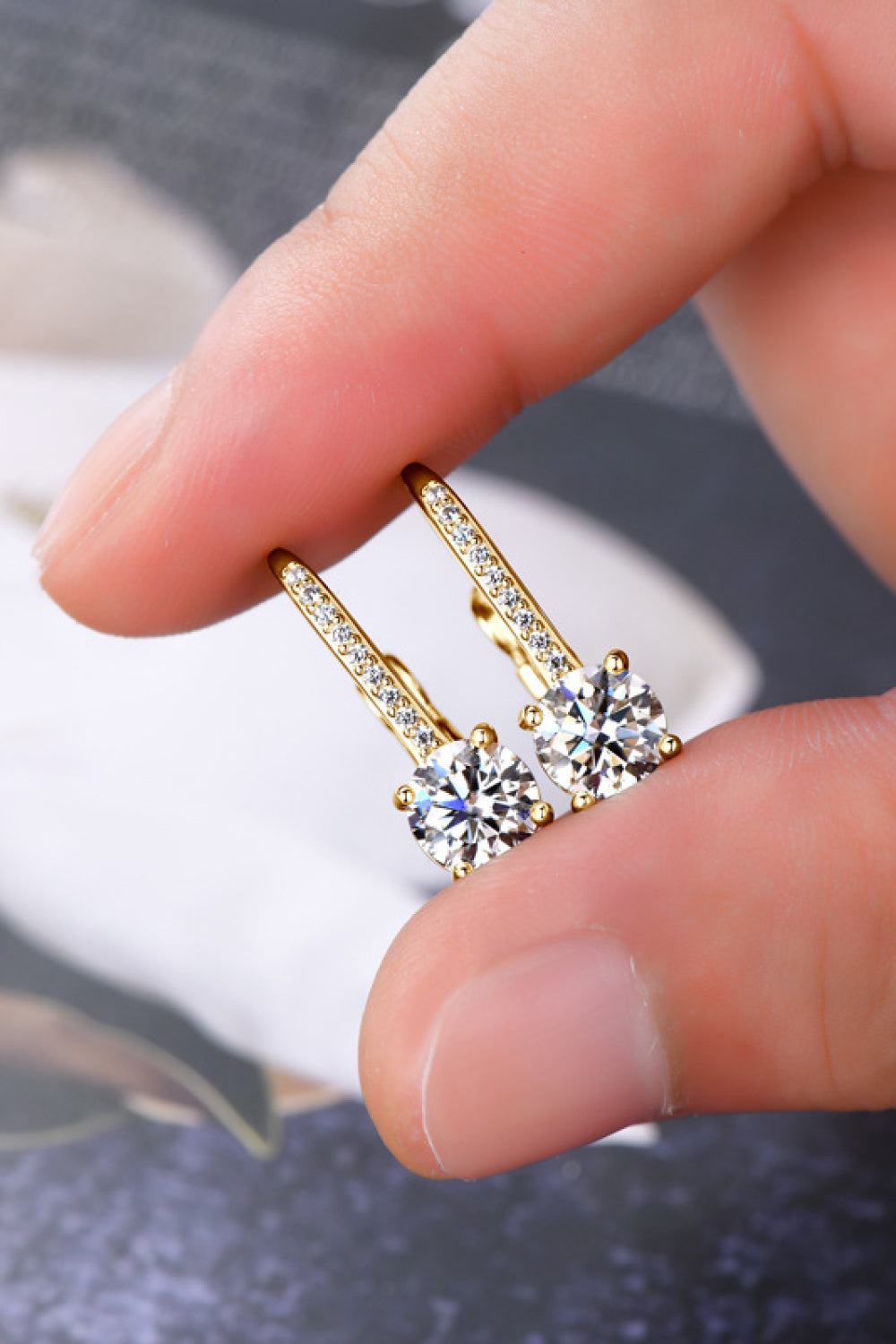 Gold earrings with clear stones held between fingers against a blurred background
