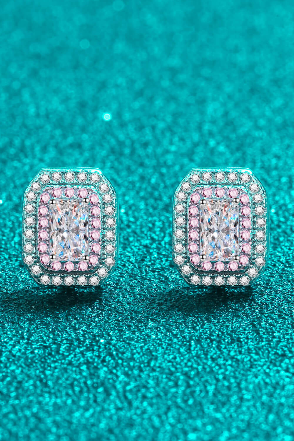Pair of diamond earrings on a teal glittery background