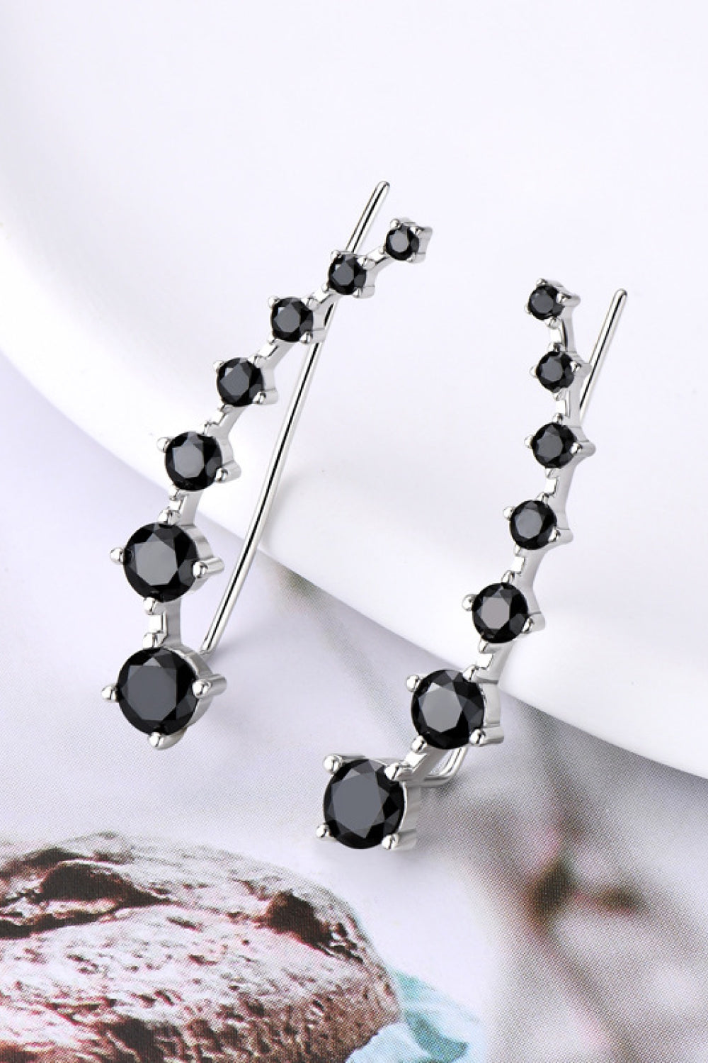 Black gemstone earrings on a white surface with a blurred background