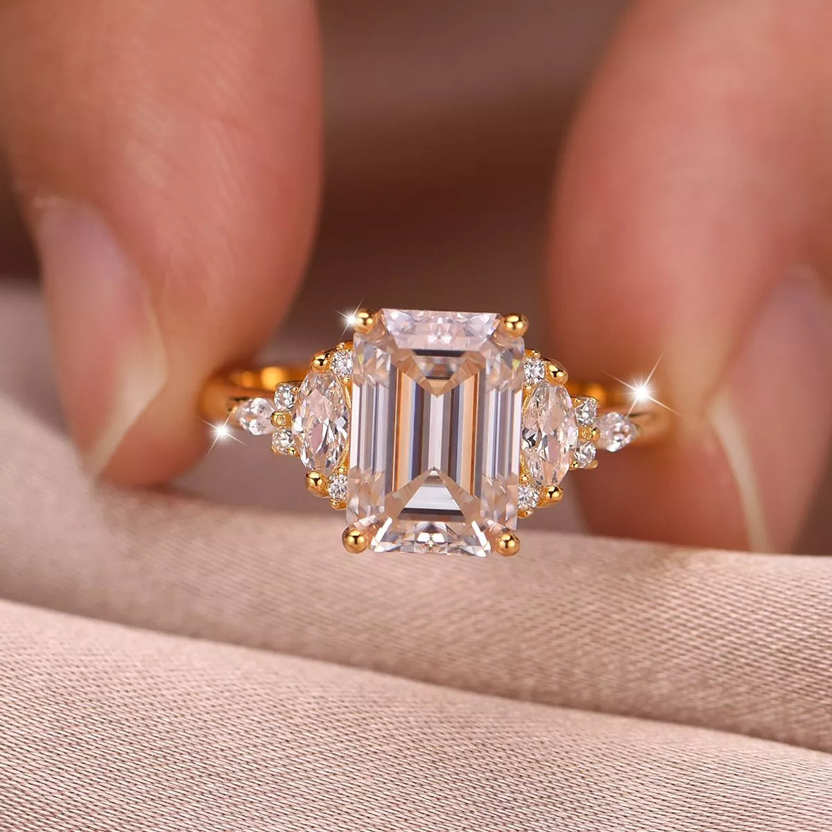 Gold ring with emerald-cut diamond held between fingers on a neutral background