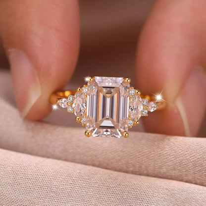 Gold ring with emerald-cut diamond held between fingers on a neutral background