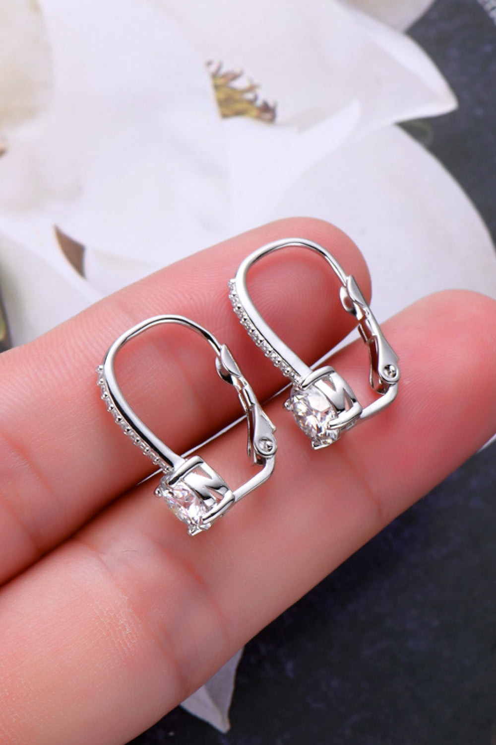Silver hoop earrings with clear gemstones held between fingers against a neutral background