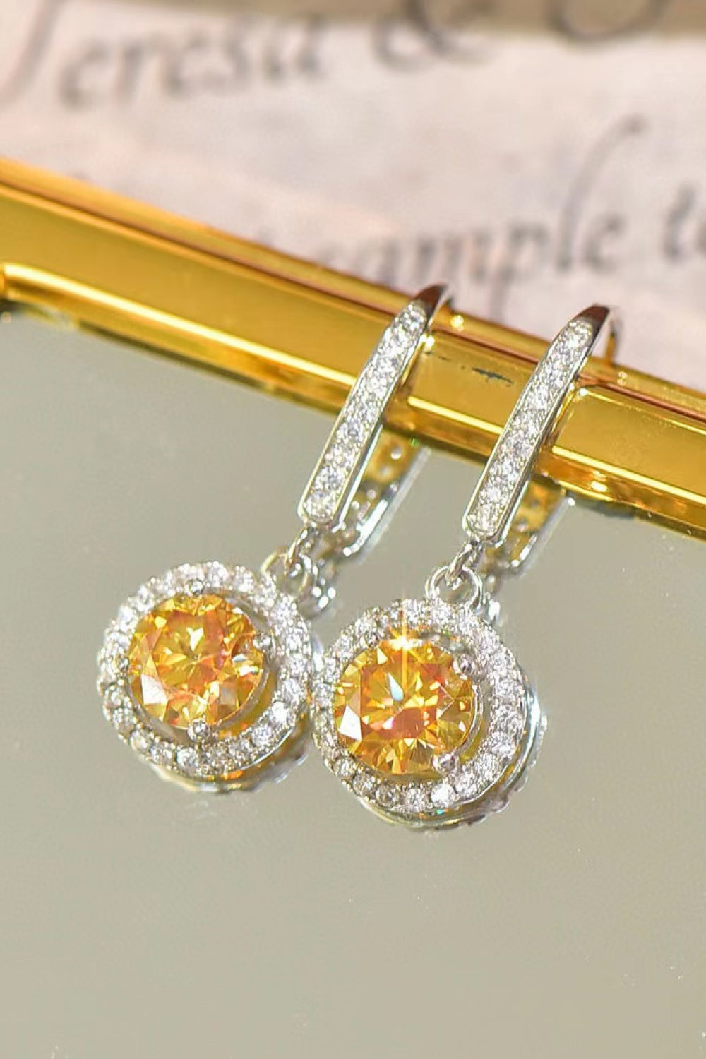 Pair of yellow gemstone earrings with silver halo on a reflective surface.