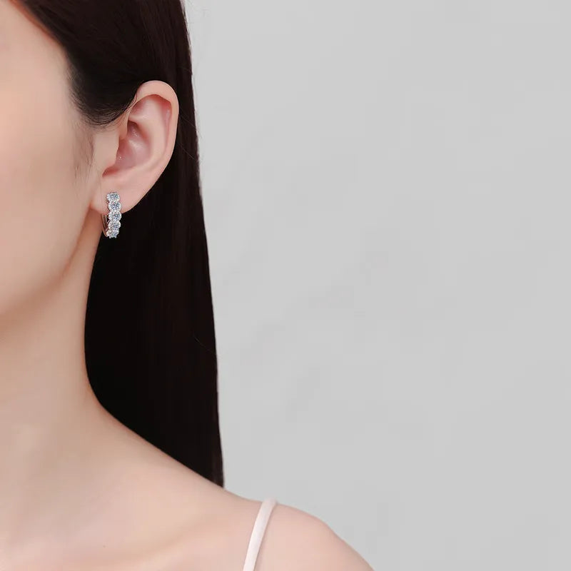 Close-up of a person wearing diamond hoop earrings on a plain background