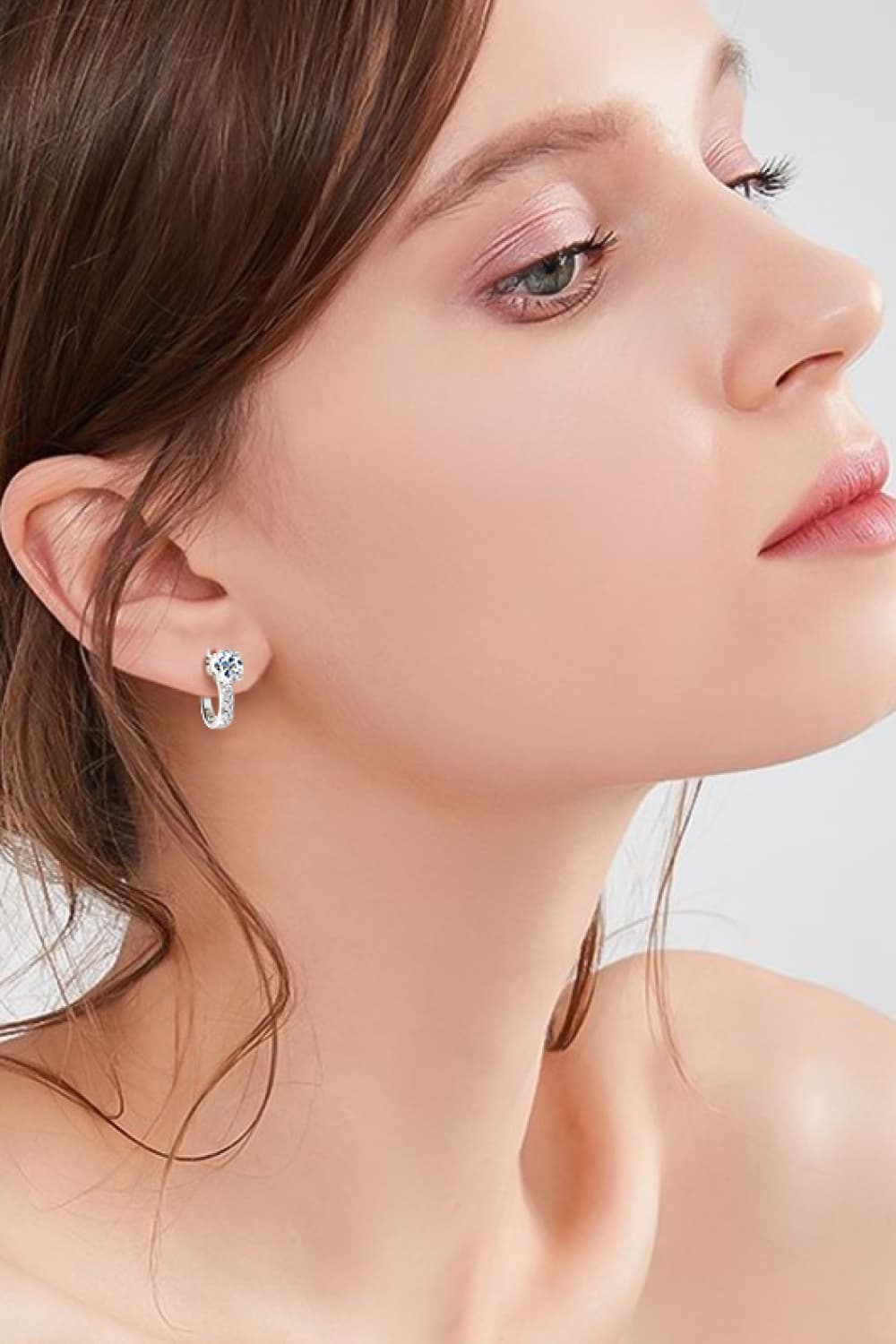 Close-up of a woman wearing a silver earring with a blue gemstone on a light background